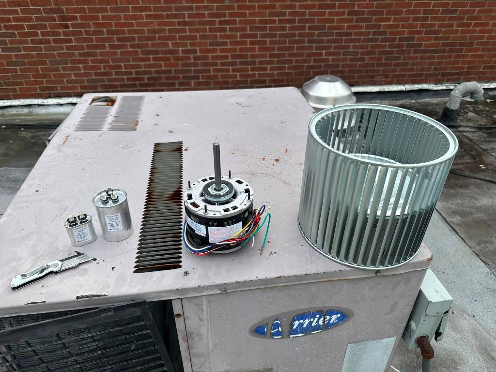 Blower wheel, motor and capacitors beside an opened rooftop unit